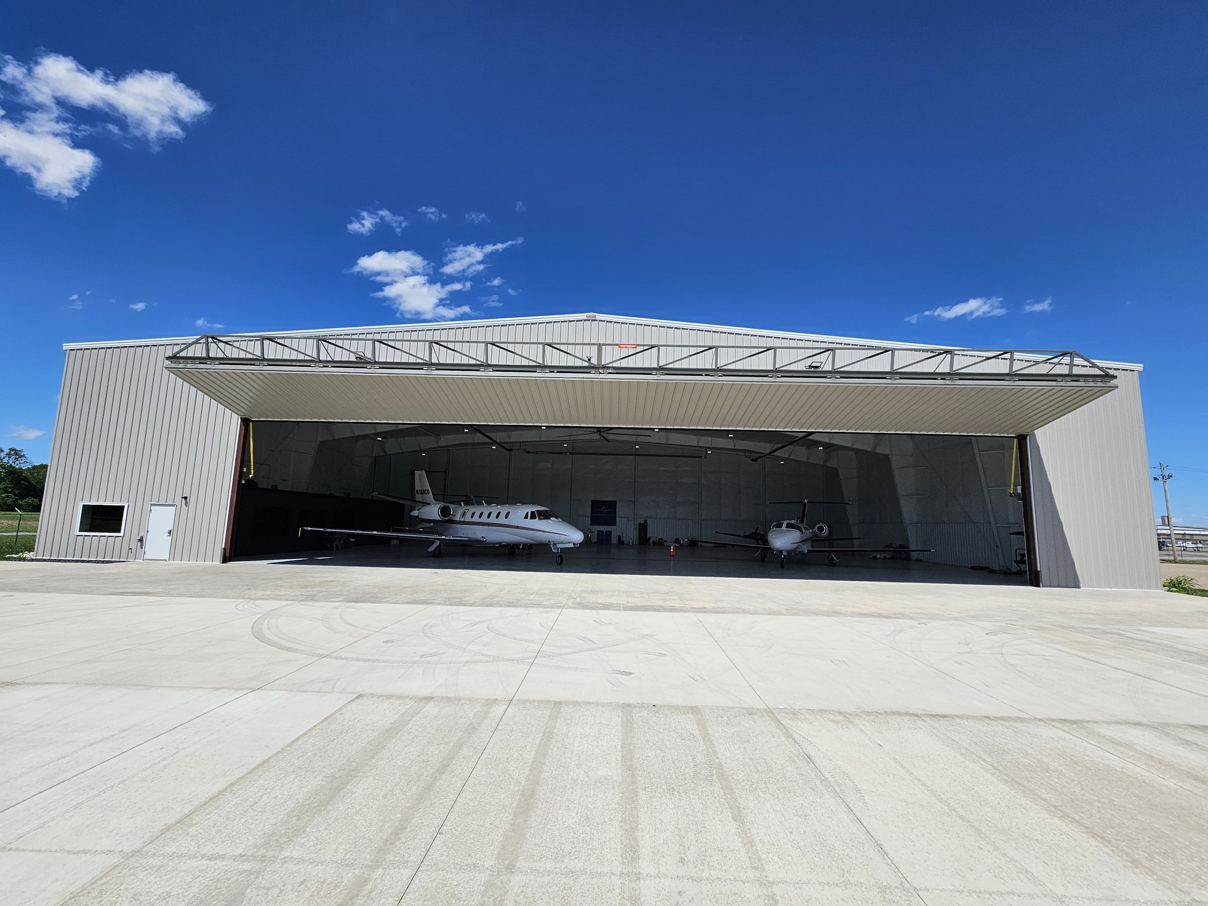 Exterior of the Gateway Jets hangar with the 100-foot bi-fold door open, a Citation Excel and Mustang inside