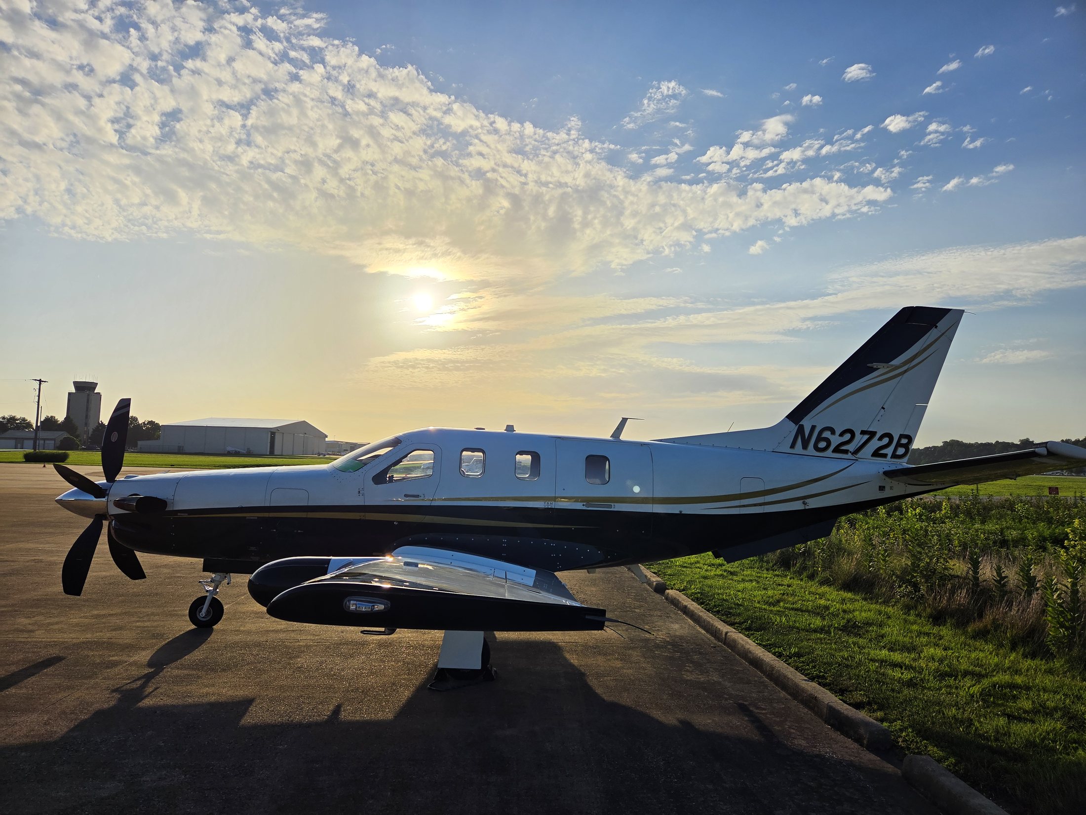 2005 TBM 700C2 N6272B in left profile with the sun breaking through high cloud behind the airport tower